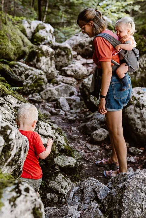 Lotte wandelt met haar kinderen een rotspad omhoog. Haar dochter zit in de draagzak op haar rug en ze kijkt achterom en wacht tot haar zoontje naar boven loopt